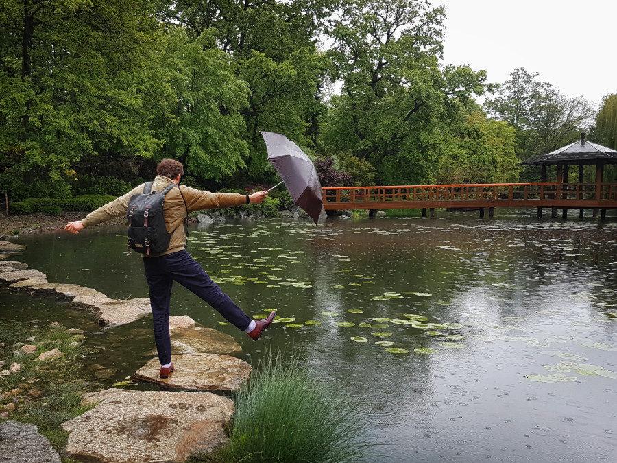Man balancing with an umbrella on the stone on the water in Japanese Garden in Wrocław, Poland