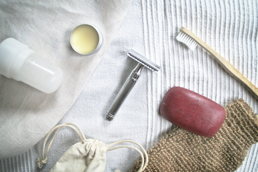 Zero Waste Beauty Routine utensils: stainless steel razor, bamboo toothebrush, natural soap bar, alum deodorant, menstrual cup laying on the cloth