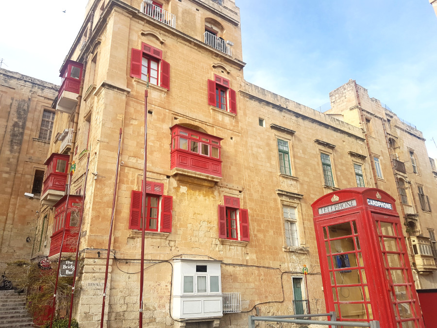 The ancient building in Valletta with a red telephone cabin in front